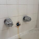 Exposed tub spout stub-out with mineral staining between dual shower handles after spout removal in Salt Lake City