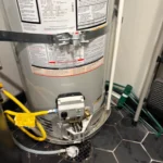 Close-up of new water heater gas valve, burner area, and floor drain after install in North Salt Lake utility room.