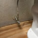 Old multi-turn bathroom angle stop and supply line at the toilet before replacement in a West Jordan bathroom.